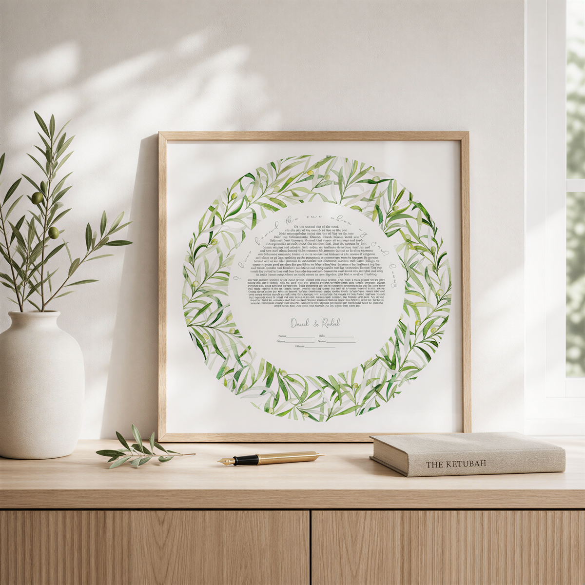 a framed document with a wreath-like border, placed on a wooden surface next to a book and a pen.